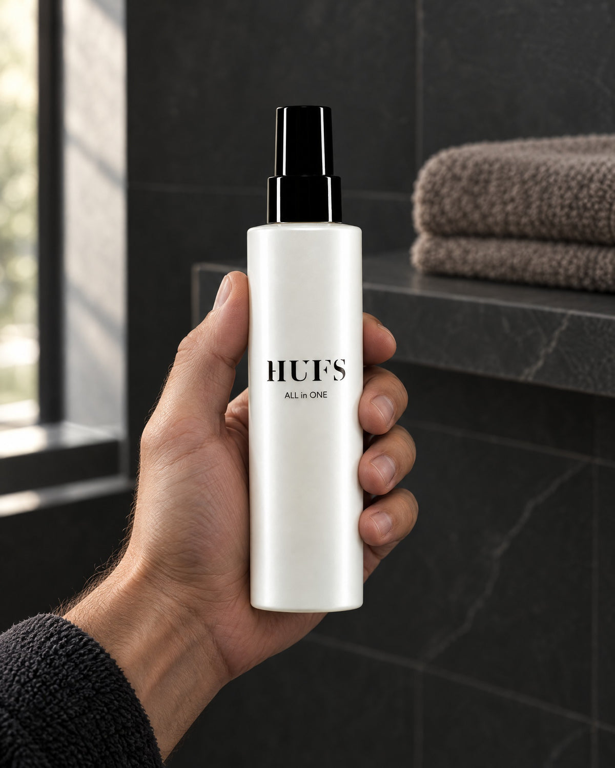 Männerhand hält HUFS All in One Leave-in Spray in einem dunklen Badezimmer mit Schieferfliesen