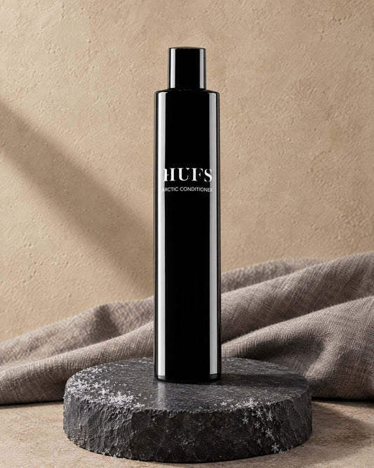 HUFS Arctic Anti-Schuppen Conditioner in glänzend schwarzer Flasche auf Schiefer-Sockel mit Raureif