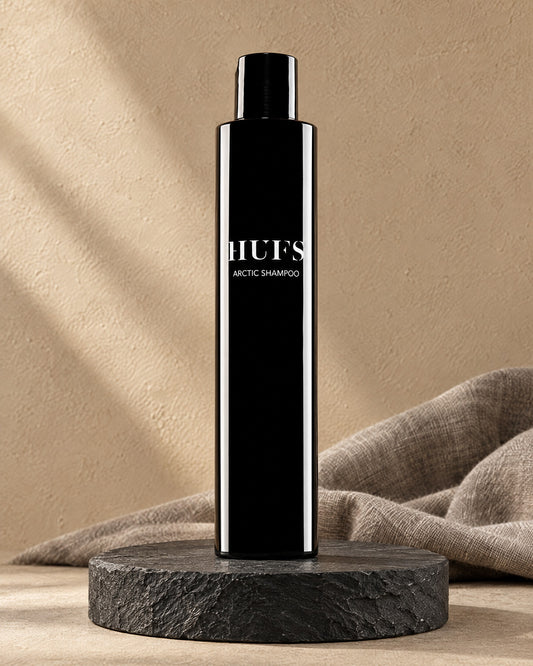 HUFS Arctic Anti-Schuppen Shampoo in glänzend schwarzer Flasche auf dunklem Schiefer-Sockel