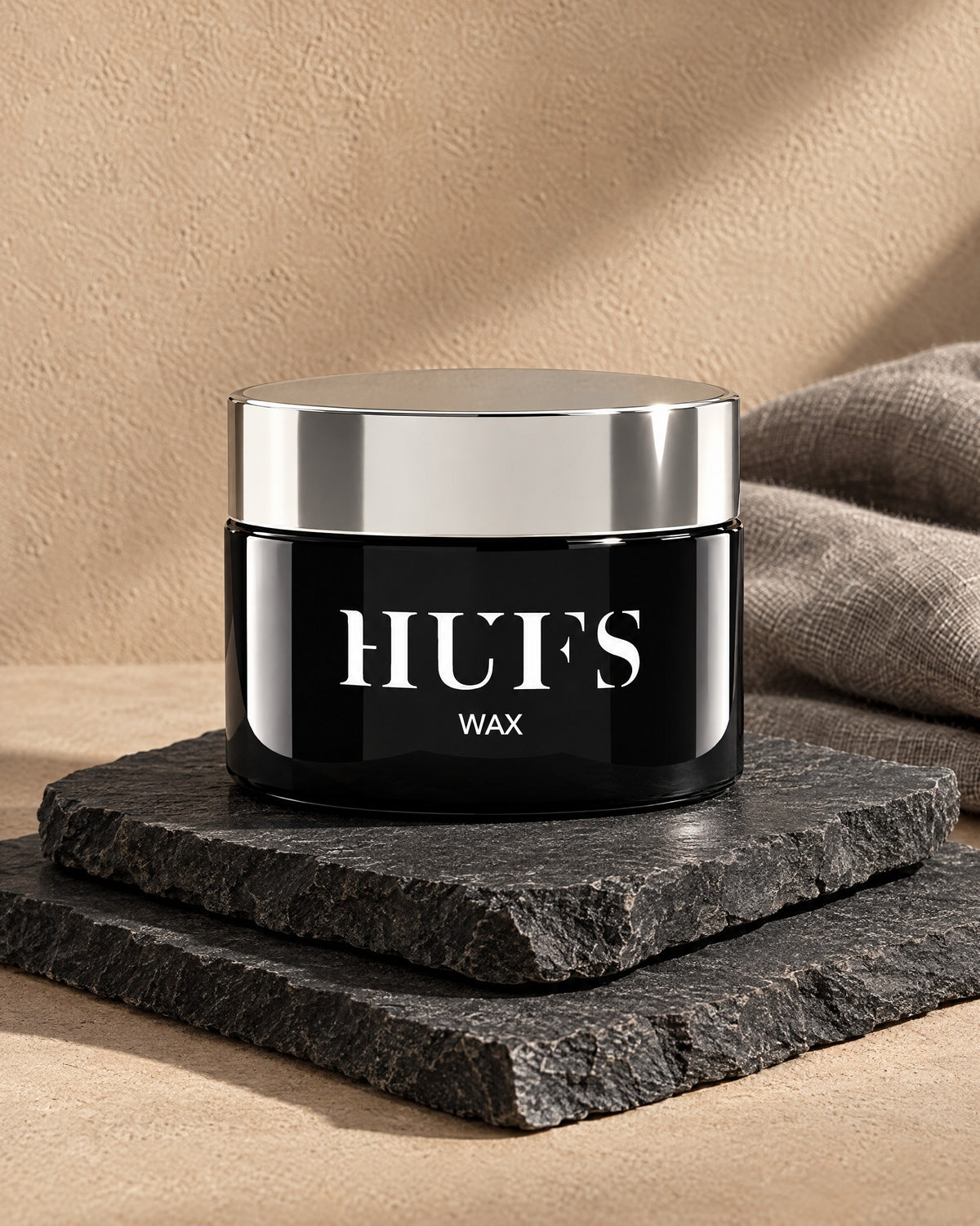 HUFS Wax 85 ml im schwarzen Tiegel mit silbernem Deckel auf gestapelten Schieferplatten