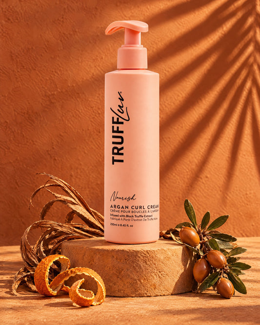 TRUFFLuv Argan Curl Cream in apricotfarbener Pumpflasche auf Sandstein mit Orangenschalen-Spiralen und Arganzweig