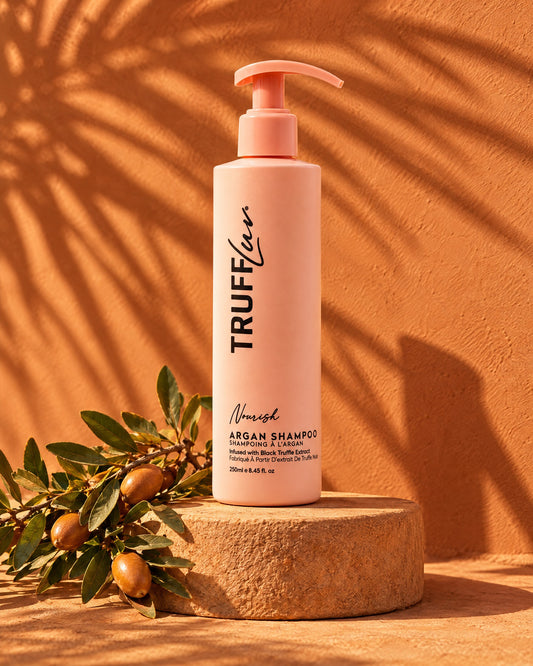TRUFFLuv Argan Shampoo Nourishing in apricotfarbener Pumpflasche auf Sandstein vor Terrakotta-Wand mit Arganzweig