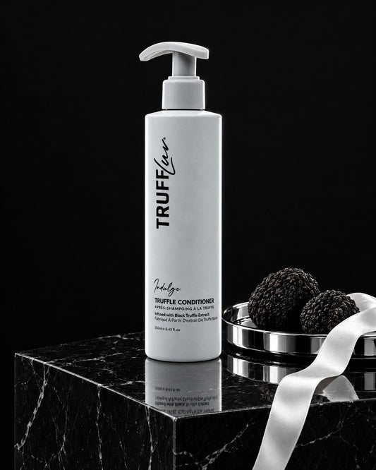 TRUFFLuv Truffle Conditioner Indulge auf schwarzem Marmorsockel neben schwarzen Trüffeln auf einer Chromschale