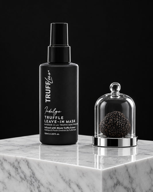 TRUFFLuv Truffle Leave-in Mask Indulge in schwarzer Sprühflasche auf weißem Marmor neben Trüffel unter Glasglocke